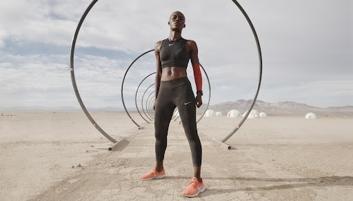 Athletic woman in sportswear posing in a desert landscape with an art installation consisting of large metal hoops, cloudy sky.