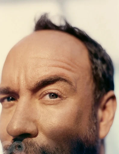 Extreme close-up of an adult man with a beard and short dark hair with fair skin in an eye-level shot against a bright background.