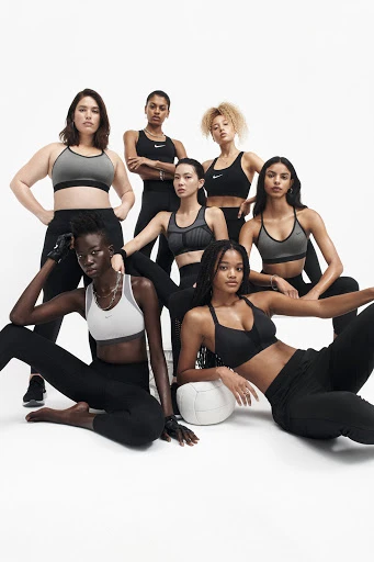 Group of diverse women posing in sports bras and leggings against a white backdrop, showcasing athletic apparel.