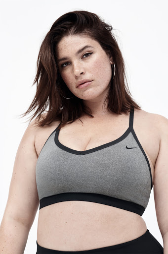 Woman in a grey Nike sports bra with black trim poses against a white background. Close-up shot of a plus-size model.
