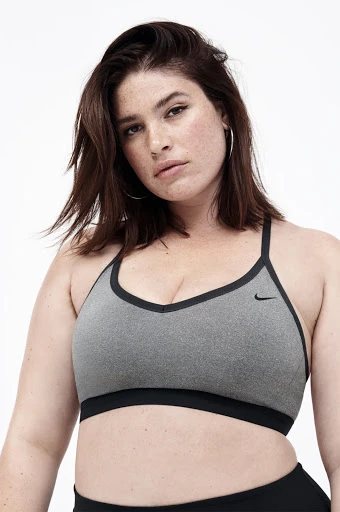 Woman in a grey Nike sports bra with black trim poses against a white background. Close-up shot of a plus-size model.