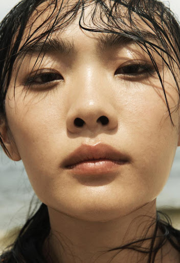Close-up portrait of an Asian female with wet hair, her skin illuminated by soft light against a blurred light-toned background.