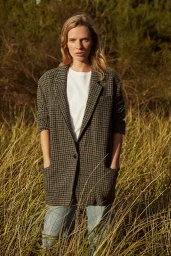 Woman in an oversized houndstooth blazer standing in tall wild grass outdoors with natural lighting
