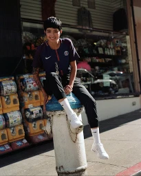 Woman with short dark hair seated on a white fire hydrant wearing a blue sports jersey, black pants, and white sneakers.