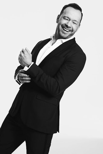 Black and white portrait of a smiling adult man wearing a black suit jacket and a white button-down shirt against a white background.