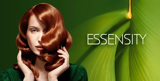 Portrait of a redhead woman with shiny, styled hair, holding hair near her face, against a green backdrop with golden oil drop.