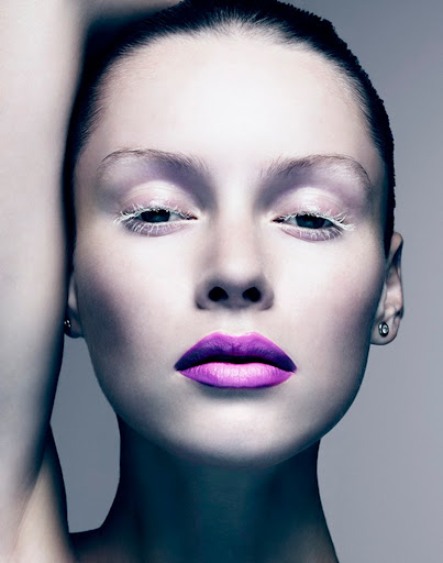 Close-up portrait of a woman with striking purple lipstick, white eyelashes, and flawless skin, showcasing beauty and makeup artistry.