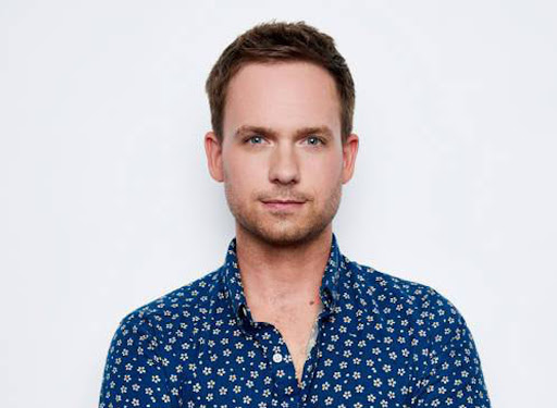 Close-up portrait of a man with brown hair and blue eyes wearing a blue shirt with white floral pattern against a white backdrop.