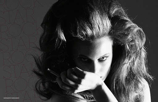 Monochrome portrait of a woman with voluminous hair, holding a cigarette to her mouth, against a blurred background with repeated text.
