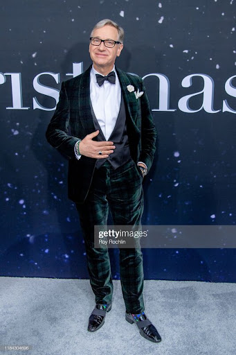 Full-length shot of a man in a dark green velvet tuxedo with a bow tie and loafers, posing against a backdrop with celestial patterns.