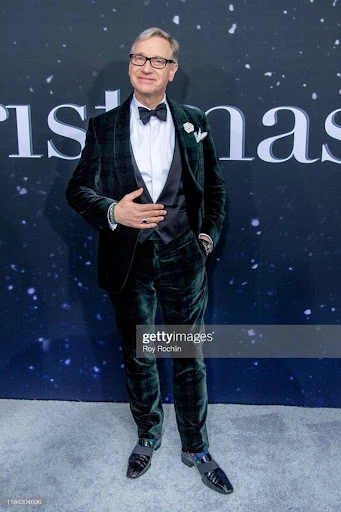 Full-length shot of a man in a dark green velvet tuxedo with a bow tie and loafers, posing against a backdrop with celestial patterns.