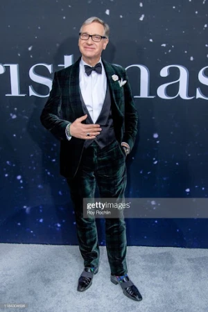 Full-length shot of a man in a dark green velvet tuxedo with a bow tie and loafers, posing against a backdrop with celestial patterns.