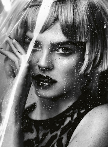 Monochrome portrait of a woman with short blonde hair looking through a glass covered in water droplets in a beauty shot.