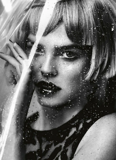 Monochrome portrait of a woman with short blonde hair looking through a glass covered in water droplets in a beauty shot.