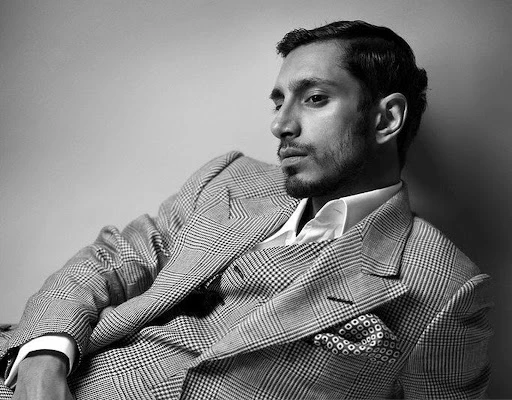 Black and white portrait of a man in a suit jacket and white shirt, looking off to the side with a serious expression.