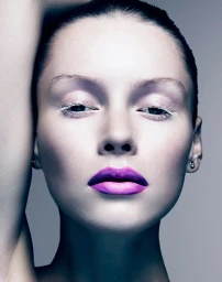 Close-up portrait of a woman with vibrant purple lipstick and white mascara on a grey seamless background