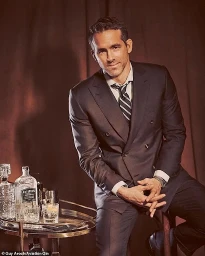 Ryan Reynolds wearing a dark double-breasted suit next to a bar cart with an Aviation Gin bottle