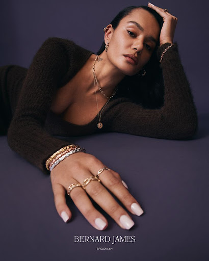 Woman in brown dress with hand jewelry and necklace in studio shot. Fashion, beauty, and jewelry advertisement with purple background.