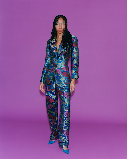 Woman in floral print suit on purple backdrop. Fashion shot features a female model wearing a colorful blazer and pants.
