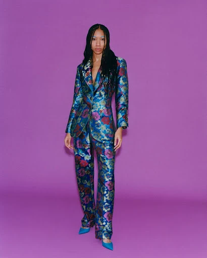 Woman in floral print suit on purple backdrop. Fashion shot features a female model wearing a colorful blazer and pants.
