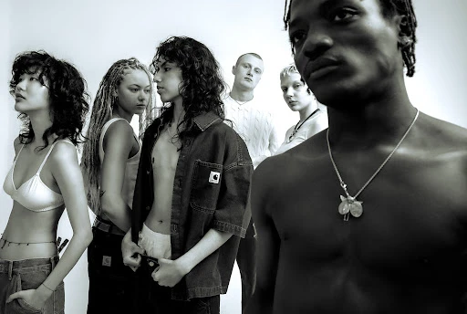Black-and-white studio shot of six models in diverse styles, including a shirtless man with a necklace, against a bright white backdrop.
