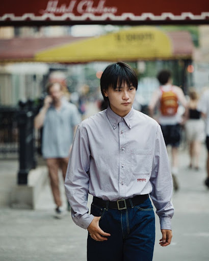Stylish short-haired woman walking on city street, wearing button-down shirt, blue jeans, and black belt in a natural setting.