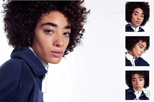 Close-up shot of a person with dark curly hair wearing a blue collared jacket against a white background in a fashion photography setting.
