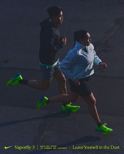 Two athletes, one male and one female, are running on pavement. They are wearing running shoes and athletic apparel in this full shot.