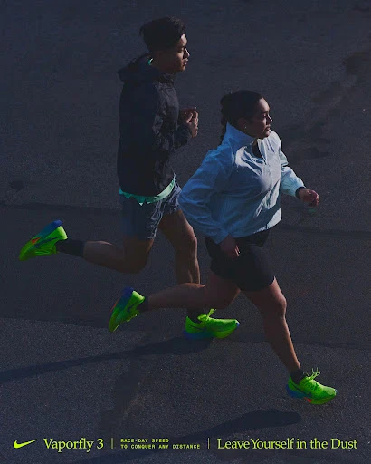 Two athletes, one male and one female, are running on pavement. They are wearing running shoes and athletic apparel in this full shot.