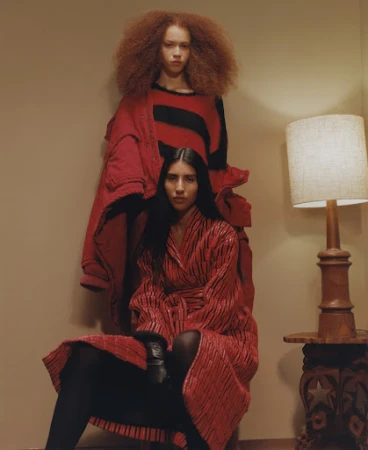 Two female models in red garments with a table lamp in an interior setting