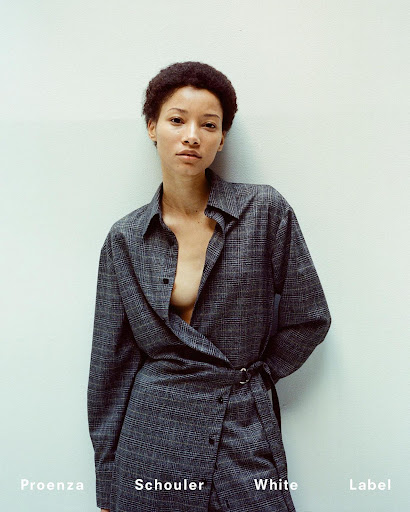 Portrait of a young adult female fashion model wearing a plaid collared button-down shirt dress against a neutral background indoors.