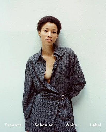 Portrait of a young adult female fashion model wearing a plaid collared button-down shirt dress against a neutral background indoors.
