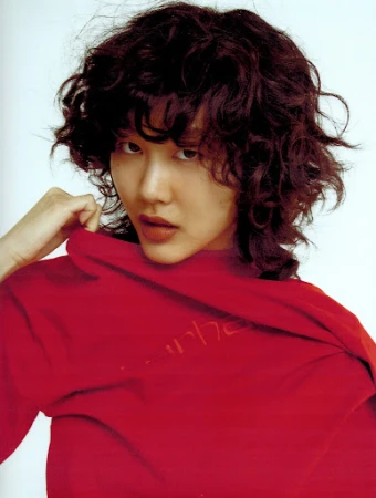 Close-up portrait of a woman with short dark curly hair wearing a vibrant red top against a white background