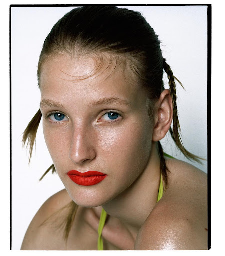 Close-up portrait of a young adult female with red lipstick, hair in braided pigtails, and a white background. Beauty and fashion.