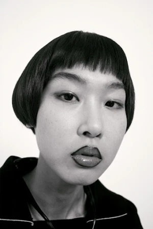 Close-up portrait of a woman with dark bob hair and distinct lip liner makeup against a white background