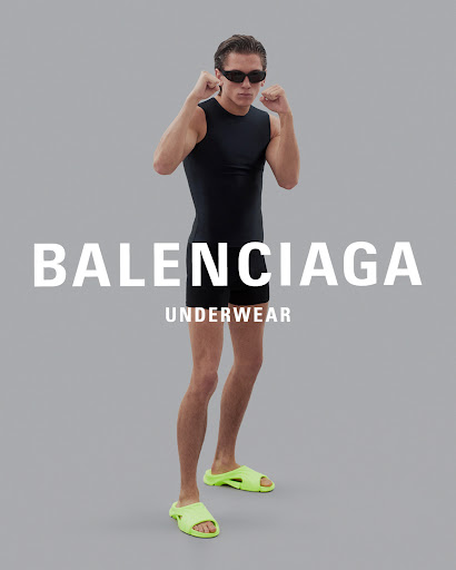 A male model poses in black athletic wear and neon slides against a gray backdrop with Balenciaga Underwear branding in front.