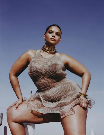 Model in a sheer pleated metallic dress posing against a clear blue sky with make-up by Camille Lutz.