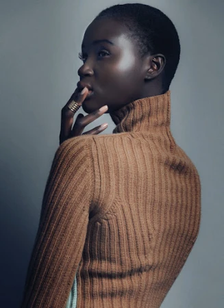 Close-up portrait of a Black woman with short hair wearing a camel-colored ribbed turtleneck and gold rings by makeup artist Camille Lutz.