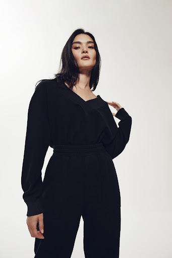Portrait of a woman in a black jumpsuit posing against a neutral background, looking at the camera with a neutral expression.
