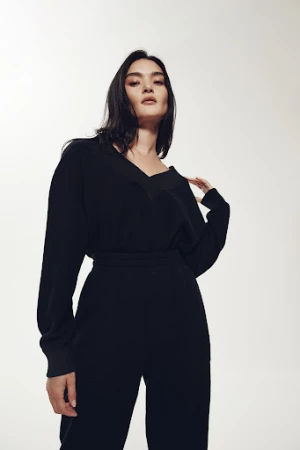 Portrait of a woman in a black jumpsuit posing against a neutral background, looking at the camera with a neutral expression.