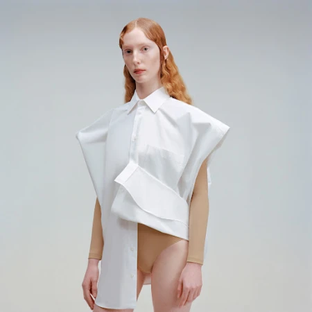 Fashion portrait of a red-haired woman wearing an oversized white shirt, posing in a photo studio with soft, neutral lighting.