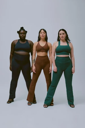 Three women pose in matching athletic wear against a neutral backdrop, showcasing different body types and styles in a studio setting.