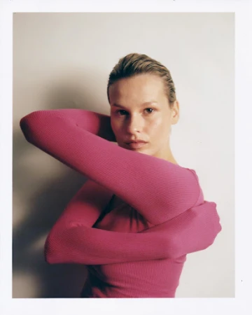 Portrait of a woman wearing a magenta ribbed long-sleeve top against a neutral off-white background.