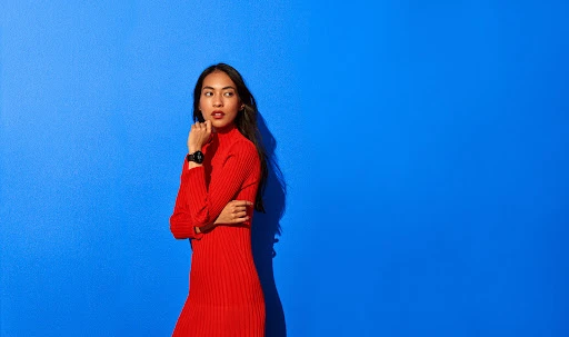 Woman in a red turtleneck dress standing against a vibrant solid blue background