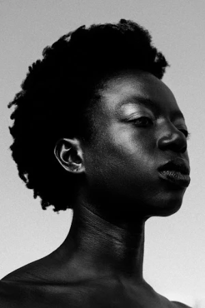 Close-up black and white portrait of a black woman with short textured hair and luminous skin posing against a light background.