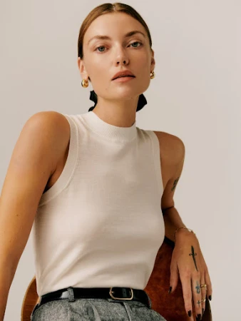Portrait of a woman wearing a white sleeveless knit top with dark hair tied back against a plain light background