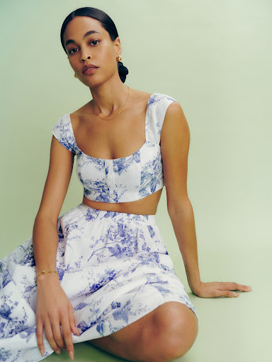 Woman in a floral crop top and skirt set poses in front of a green backdrop, showcasing a fashion-forward and feminine style.