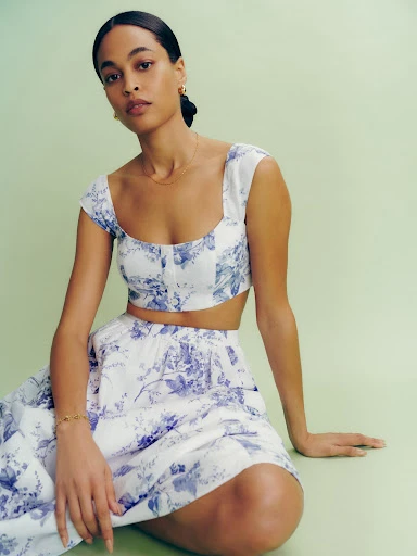 Woman in a floral crop top and skirt set poses in front of a green backdrop, showcasing a fashion-forward and feminine style.