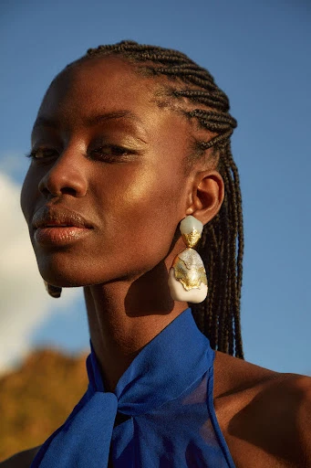 Close-up of an African woman in royal blue with striking gold earrings against a blue sky. Beauty and fashion portrait.