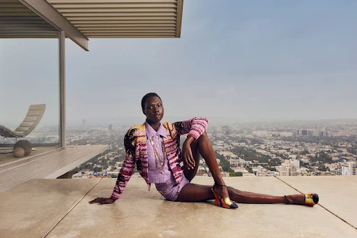 Stylish woman poses in jacket and shorts with a city view from a modern building, emphasizing fashion and urban elegance.